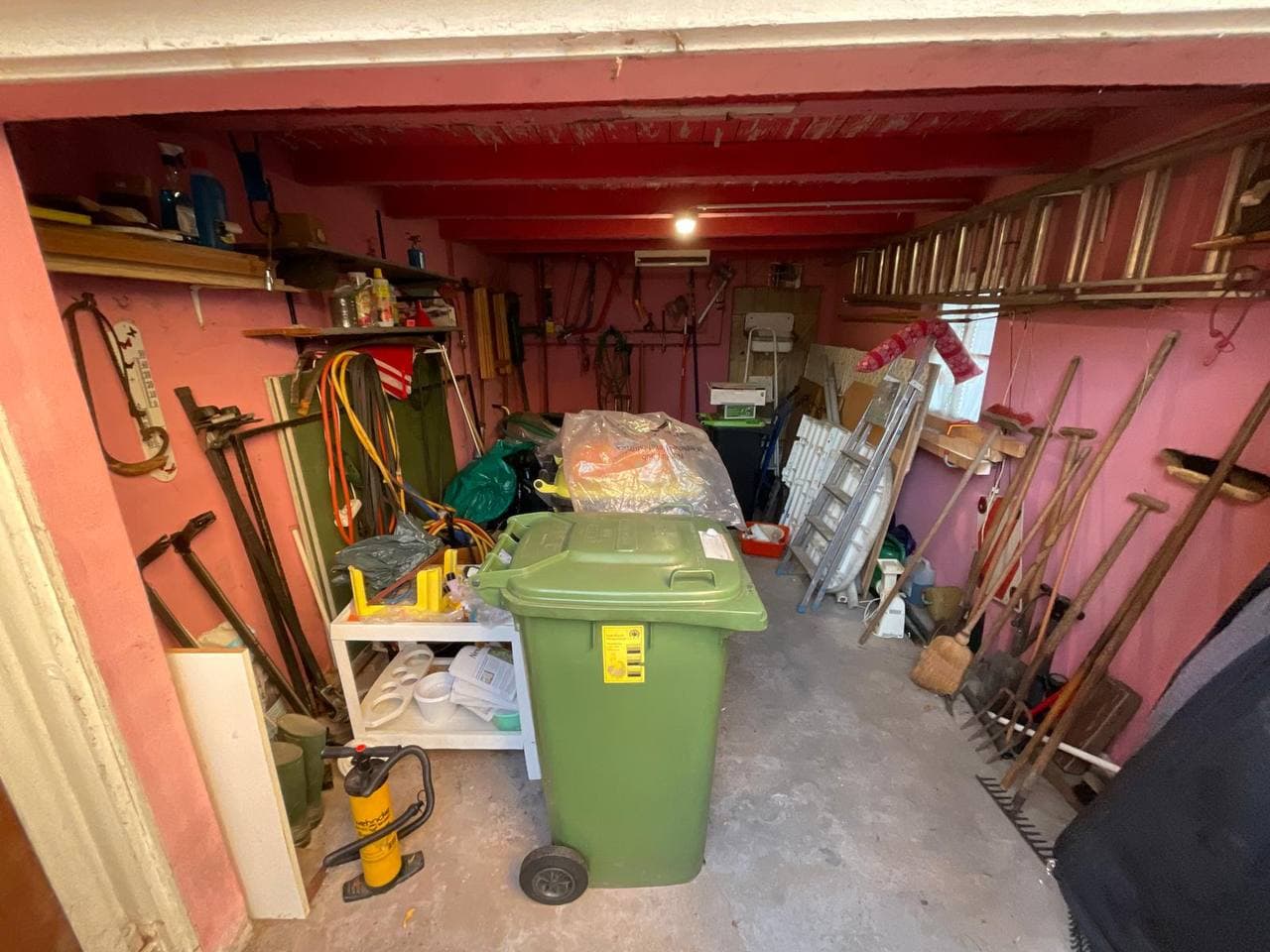 Volle Garage mit Werkzeug, Gartengeräten und Mülltonne vor der Räumung